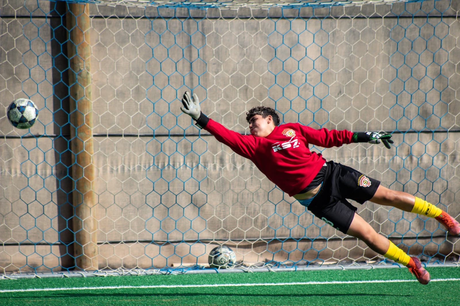 A young goalkeeper diving to catch a soccer ball