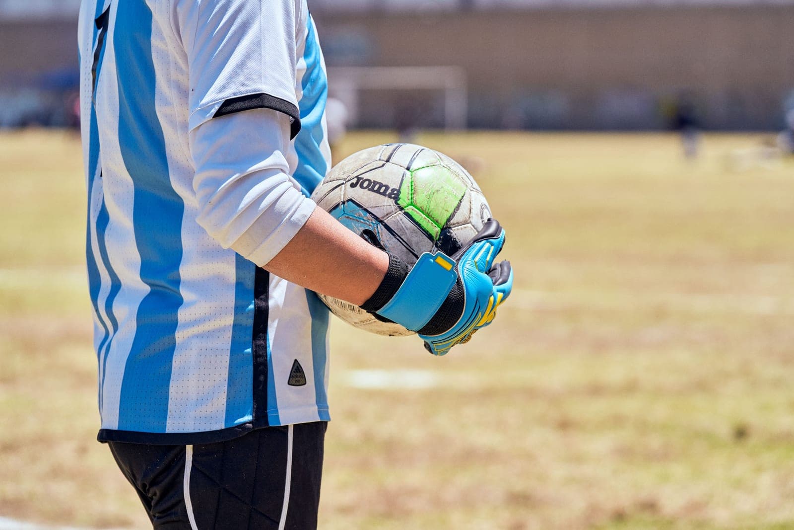 A young goalkeeper holding a soccer ball in gloved hands